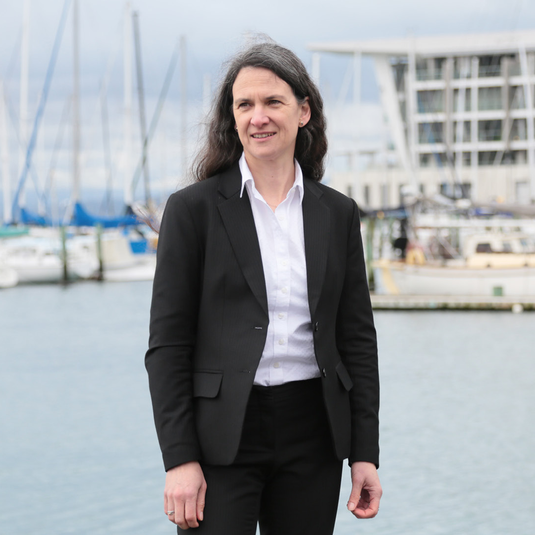 Barbara Nebel in a black suit standing in front of a harbour with boats in the background